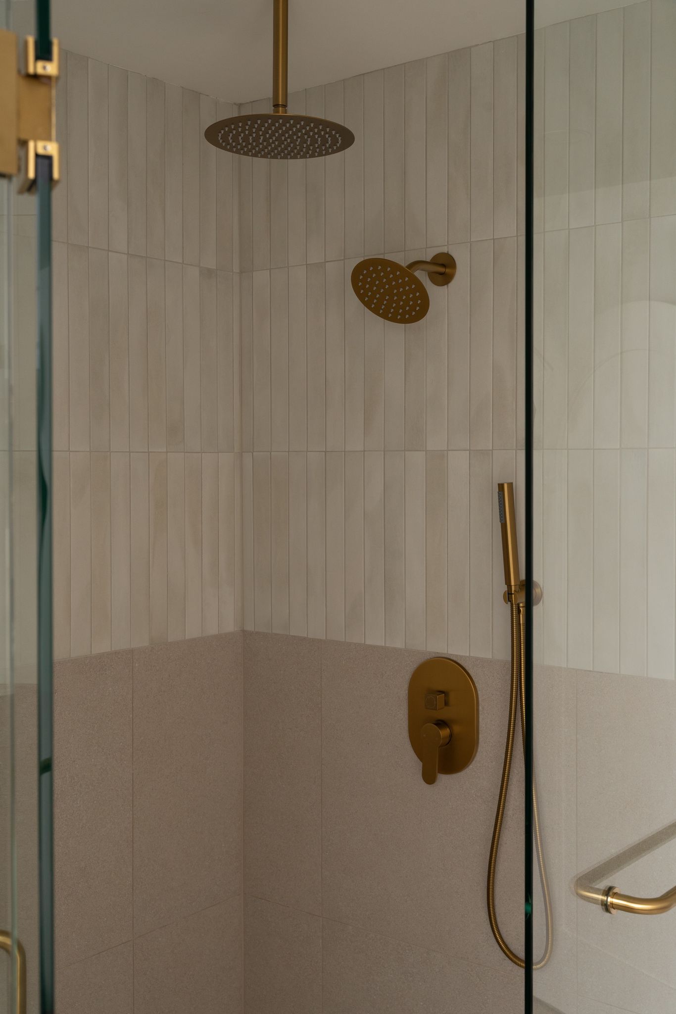 Primary washroom shower with vertical tile and brushed brass fixtures